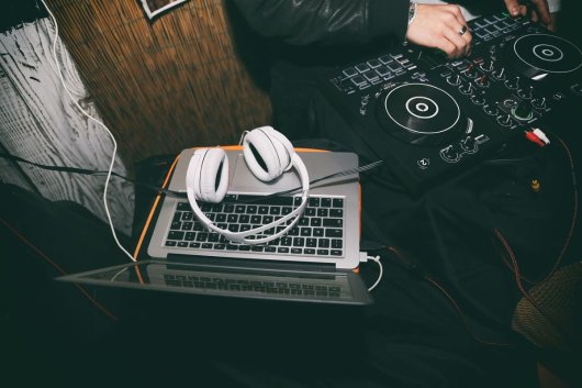Un portátil junto a un DJ que está pinchando música con una mesa de mezclas