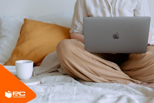 Chica sentada en la cama con un ordenador portátil y un café