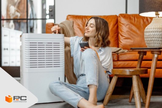 Una chica sentada en el suelo junto a un aire acondicionado portátil